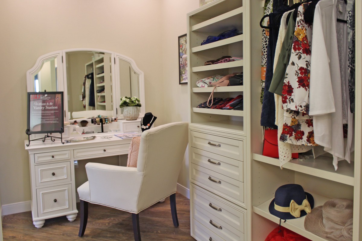 A well-organized dressing room featuring a vanity with a mirror, a comfortable chair, and neatly arranged shelves of clothing.