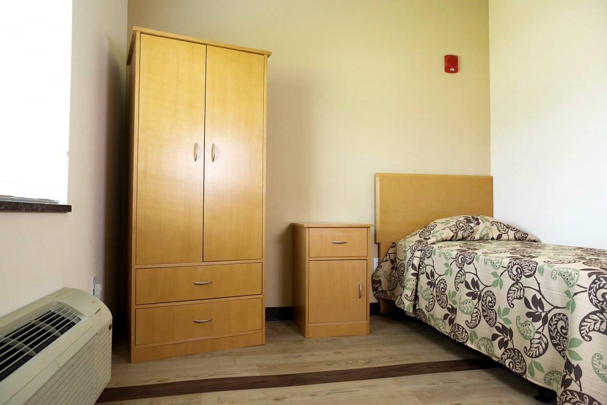 A simple bedroom setup with a wooden wardrobe, nightstand, and bed.