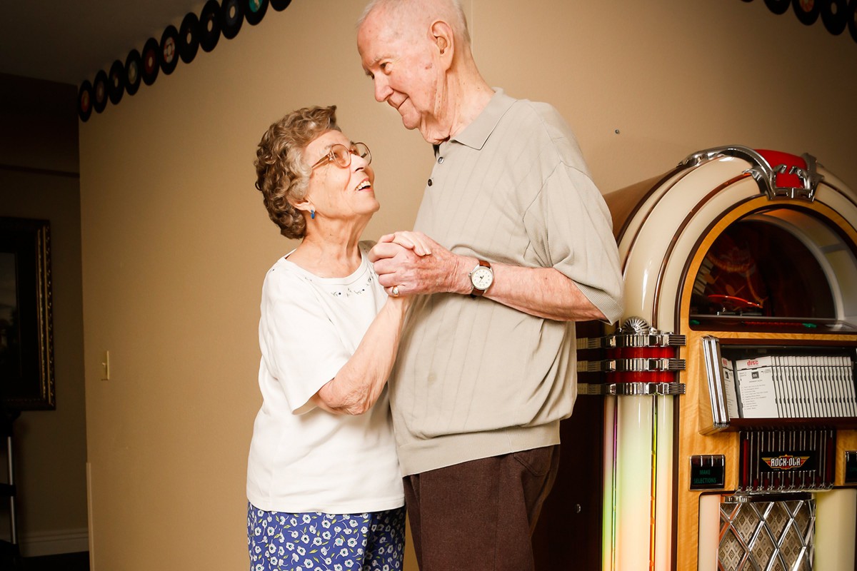 An elderly couple shares a joyful dance next to a jukebox.