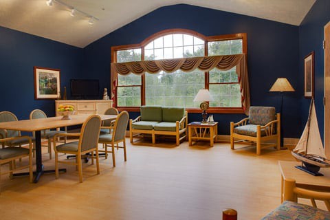 A cozy living room area with large windows, featuring sofas, chairs, and a table.