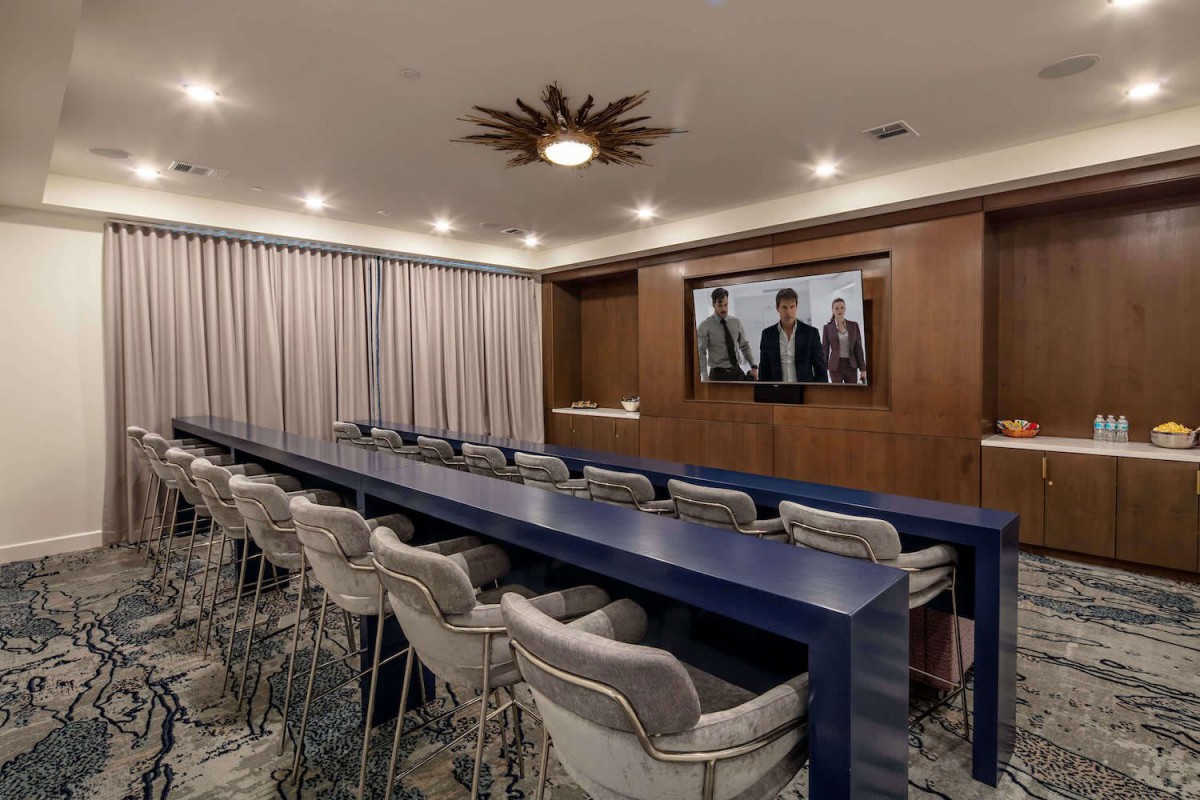 A modern conference room featuring a long table, comfortable chairs, a large screen, and stylish wood paneling.