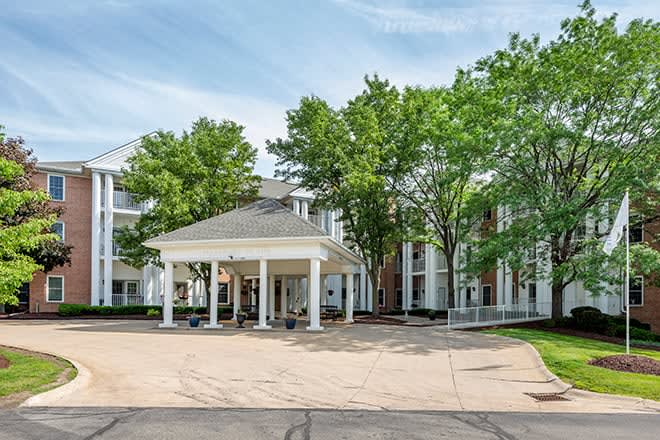 A spacious building entrance surrounded by trees with a wide driveway.