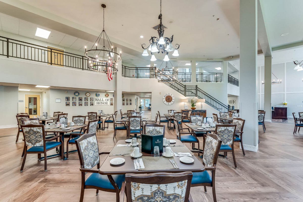 An elegant dining area with beautifully arranged tables and chairs, illuminated by chandeliers.