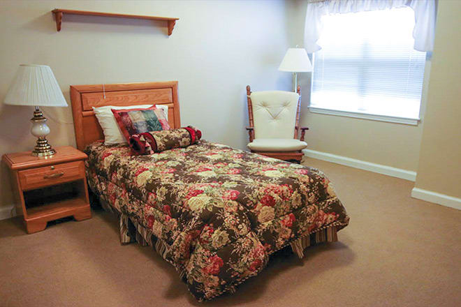 A cozy bedroom with a floral bedspread, a rocking chair, and a window.