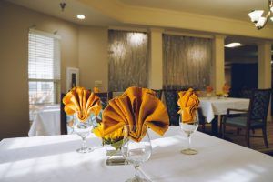 An elegantly set dining table in a restaurant with intricately folded orange napkins in wine glasses.