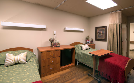 A shared hospital room featuring two patient beds, wooden furniture, and soft lighting.