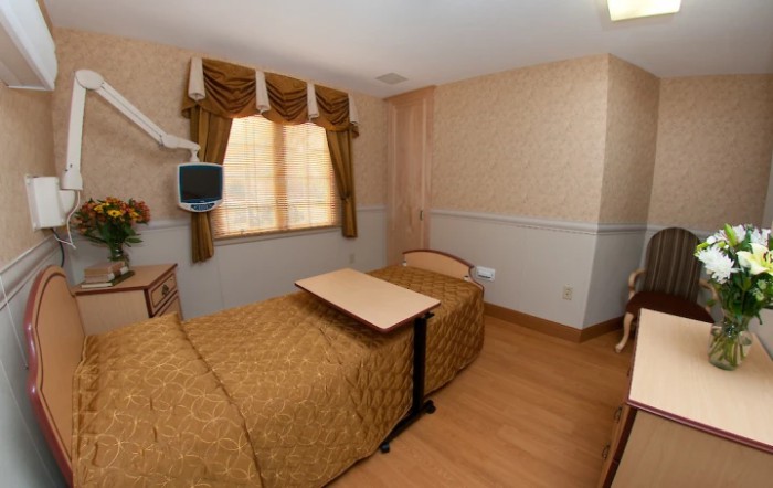 A hospital room with a single bed, TV, and wooden flooring.