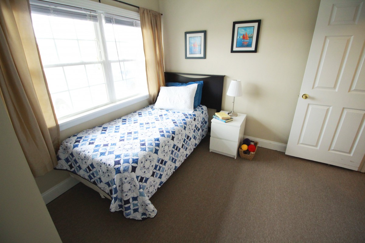 A cozy bedroom with a single bed, blue and white bedding, and plenty of natural light from the window.
