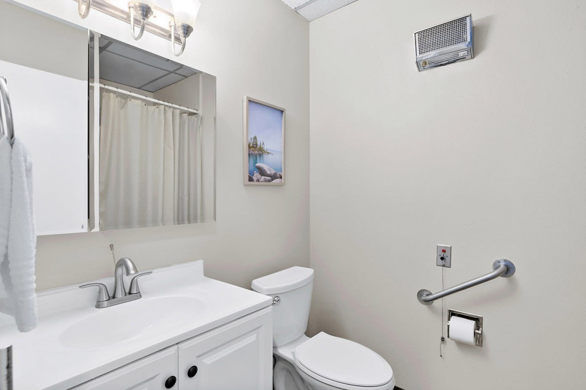 A modern bathroom with a sink, toilet, mirror, and wall art.