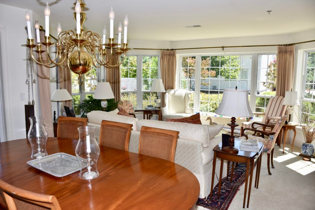 A spacious living and dining area with a wooden table, elegant chandelier, and large windows providing ample natural light.