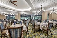 A spacious, elegantly decorated dining room with multiple tables and chairs, featuring chandeliers and large windows.