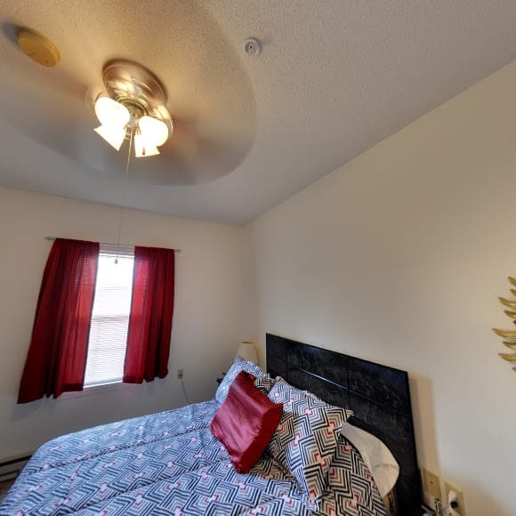 A cozy bedroom with a bed, red curtains, and a ceiling fan.