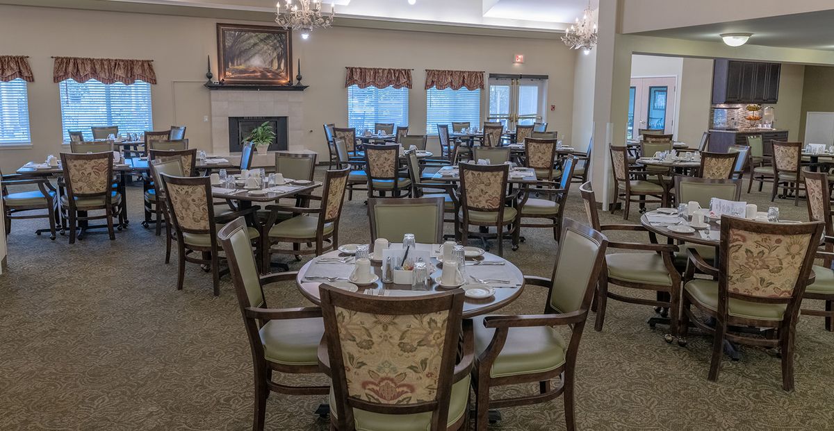 An elegant dining room with set tables and ornate chairs, illuminated by chandeliers.