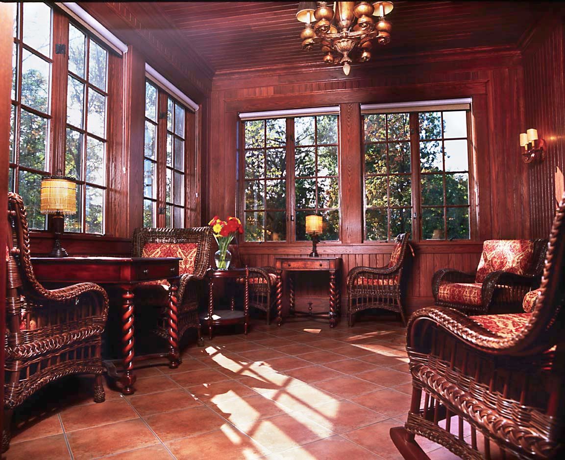 A cozy room with wooden paneling, wicker furniture, and abundant natural light streaming through large windows.