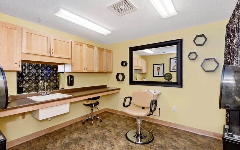 A well-lit hair salon station with a chair, large mirror, and wooden cabinets.