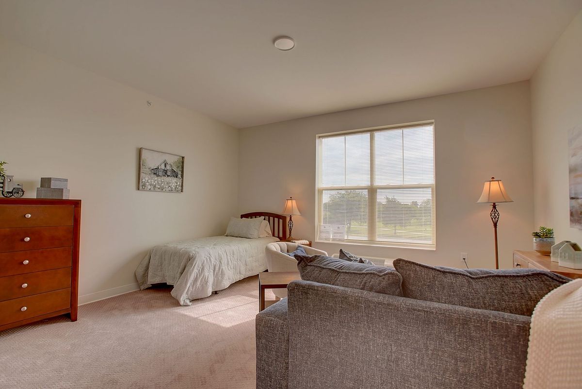 A cozy bedroom with a single bed, large window, and comfortable seating.