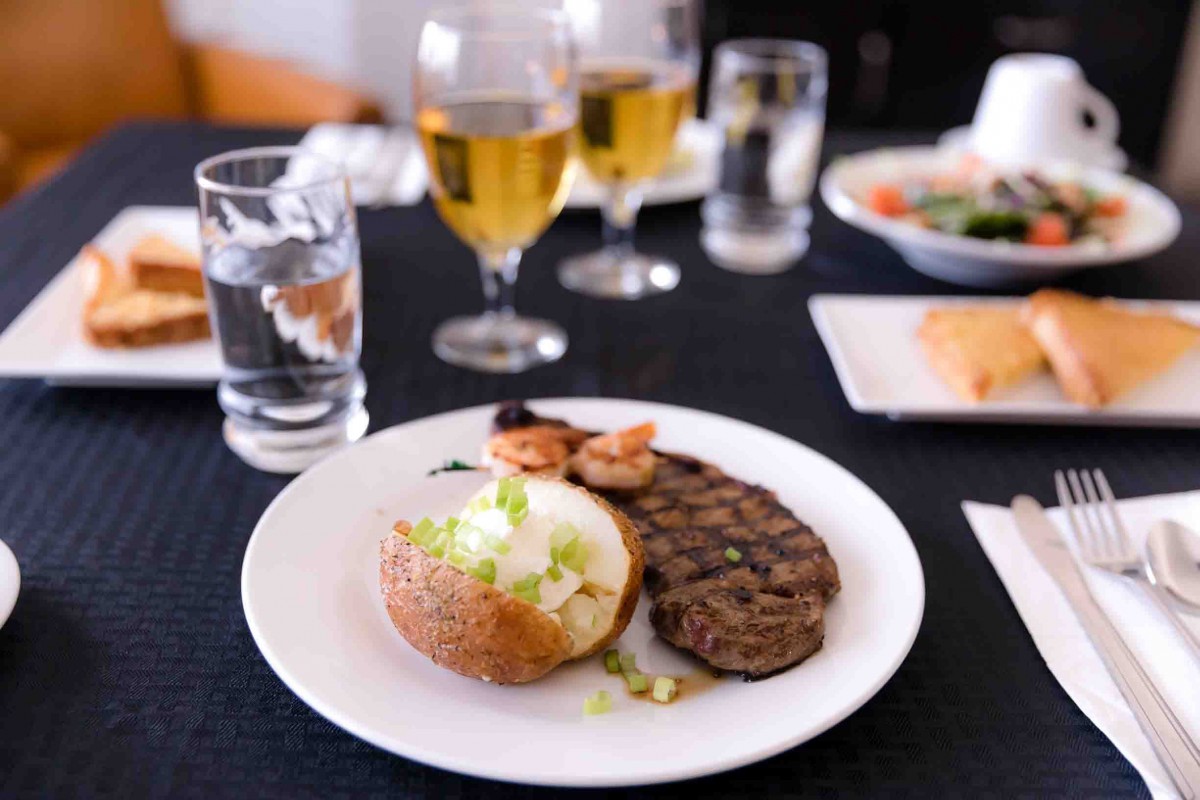 A plate of steak, shrimp, and a baked potato served with drinks on a restaurant table.