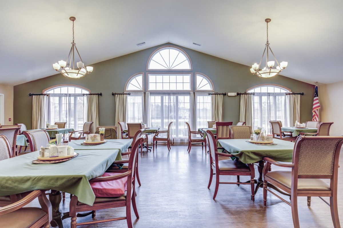A bright and spacious dining room with multiple tables and chairs, illuminated by natural light streaming through large windows.