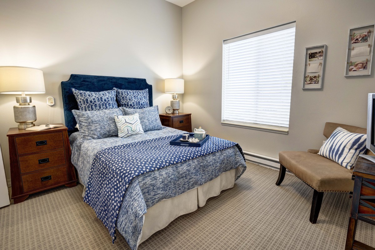 A cozy bedroom with a neatly made bed, bedside tables with lamps, and a window letting in natural light.