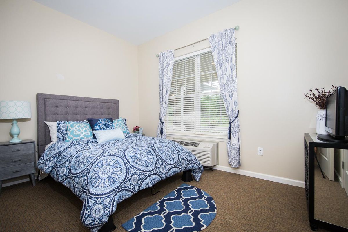 A cozy bedroom featuring blue patterned bedding and matching curtains, with a window providing natural light.