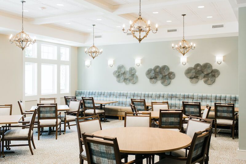 A beautifully decorated dining room with round tables, chairs, and elegant chandeliers.
