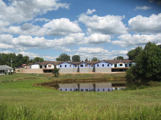 A serene view of residential houses reflected in a pond under a cloudy sky.
