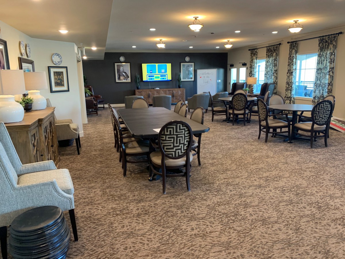 A spacious dining area with neatly arranged tables and chairs, featuring a television and elegant lighting.