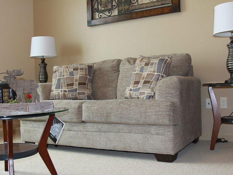A cozy living room with a beige sofa, patterned pillows, a stylish coffee table, and a lamp.