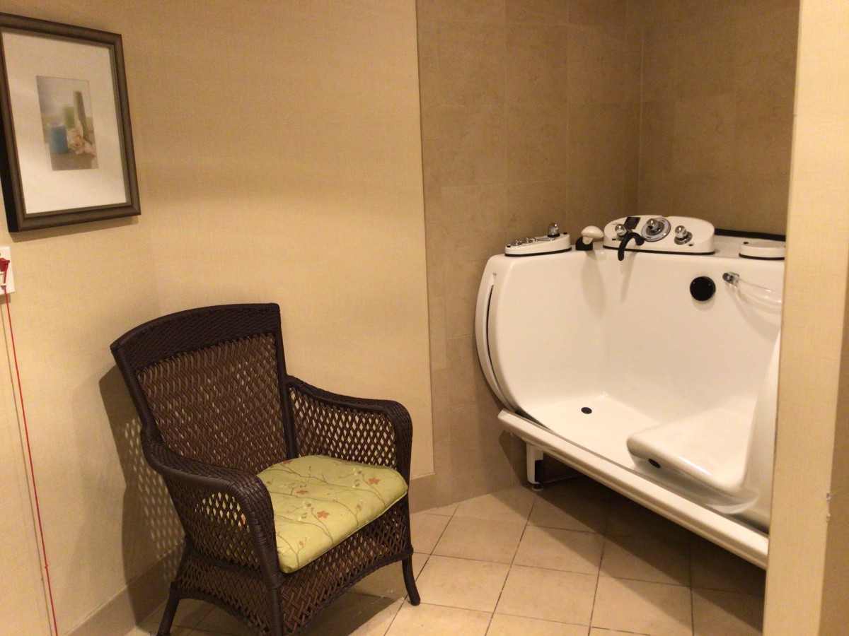 A bathroom featuring a wicker chair and a walk-in bathtub against beige walls.