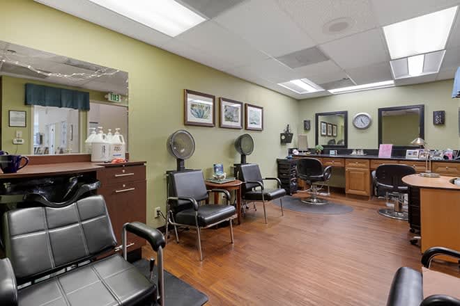 A cozy hair salon with seating, mirrors, and hairdryers, featuring a wooden floor and calming decor.