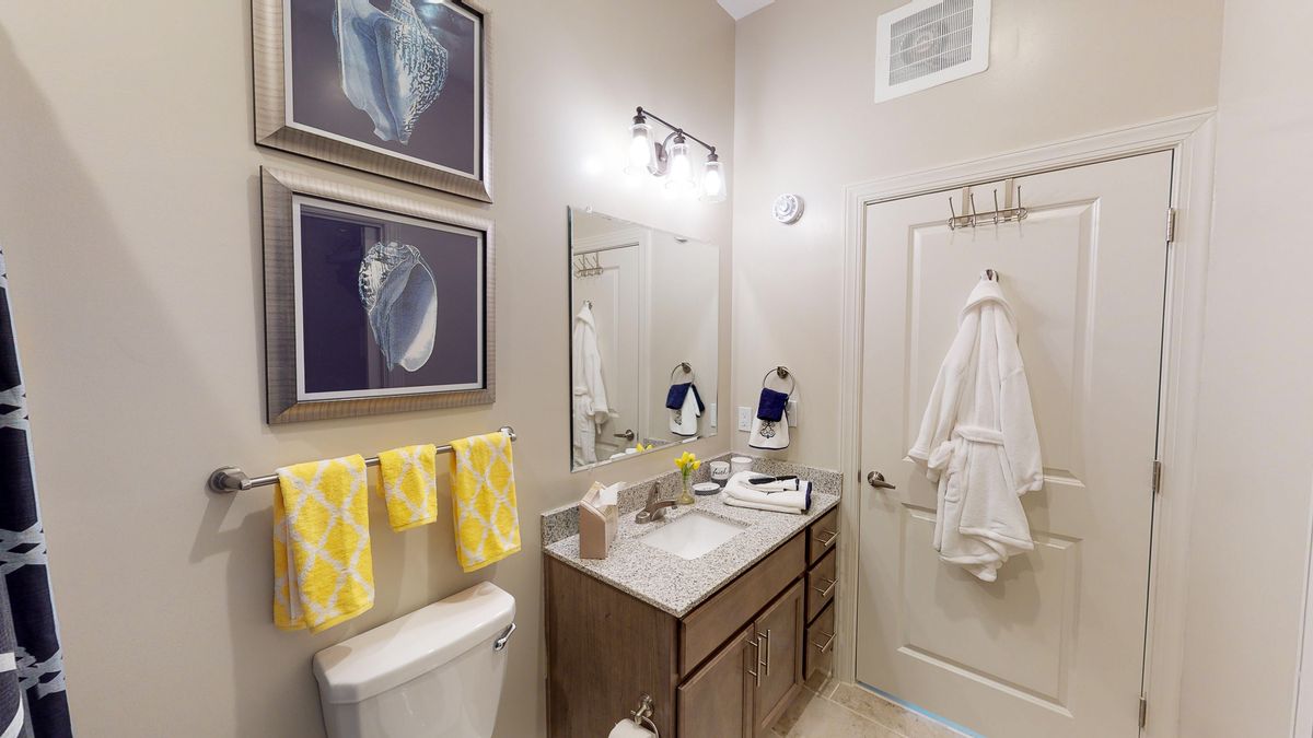 A well-organized bathroom featuring a vanity with a mirror, bright yellow towels, and artistic wall decor.