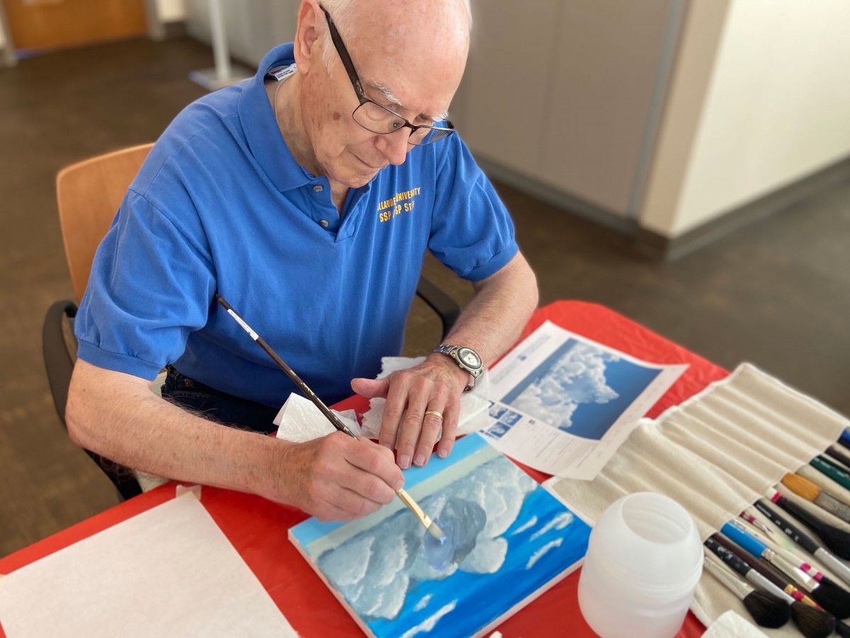 An elderly person painting a landscape indoors.