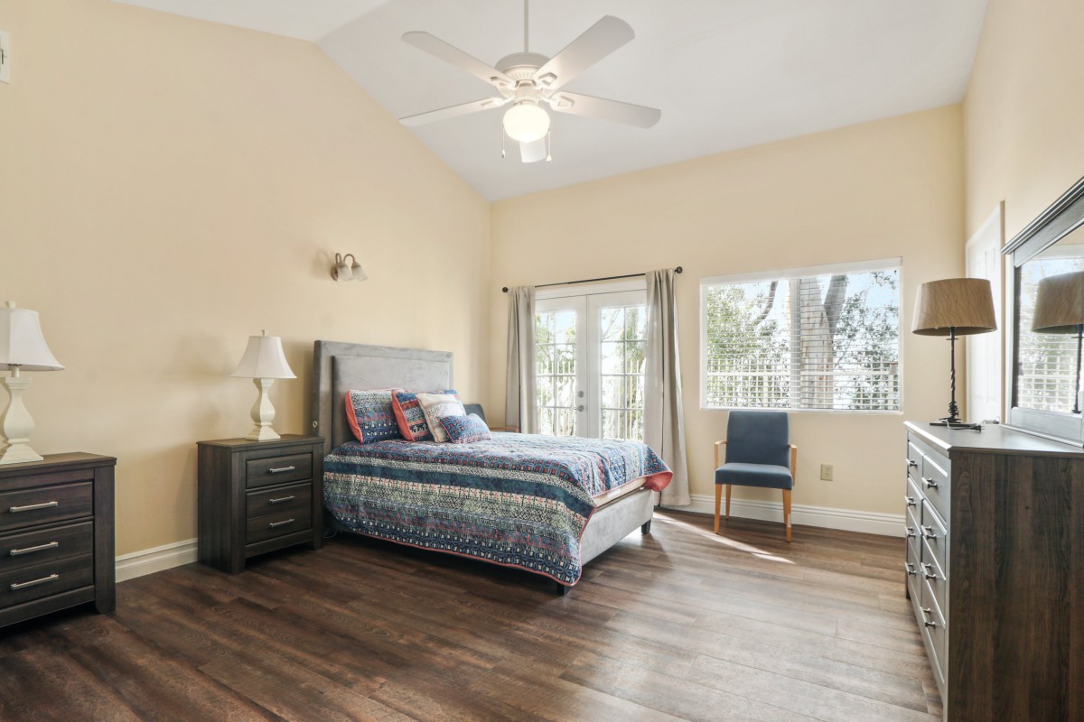 A spacious modern bedroom with wooden flooring, a large bed, and abundant natural light from the windows.