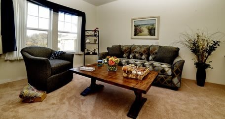 A cozy living room featuring a comfortable sofa and a wooden coffee table adorned with flowers, set against a backdrop of neutral tones and tasteful decor.