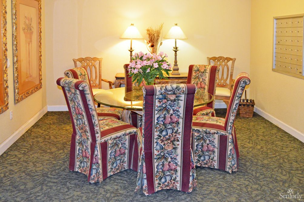 A cozy dining area featuring a round table surrounded by chairs with floral upholstery, adorned with a floral centerpiece and illuminated by warm lighting.