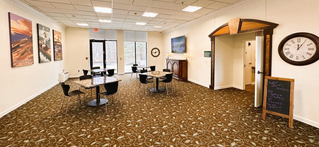 A spacious lobby area with tables and chairs, featuring a television and large windows.