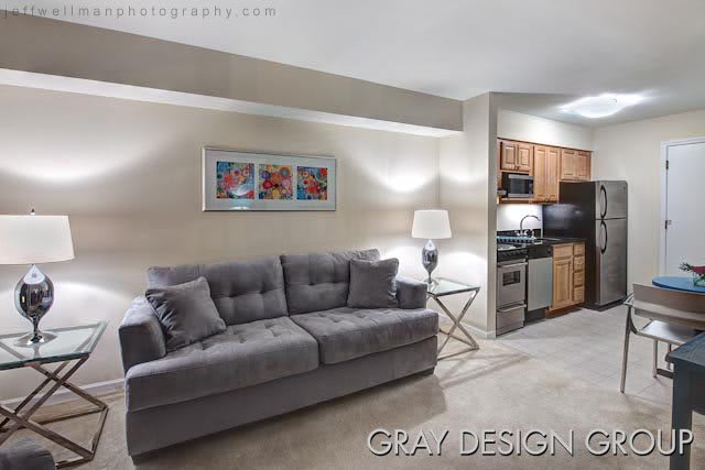 A modern living space featuring a gray sofa, decorative artwork, and an open kitchen area.