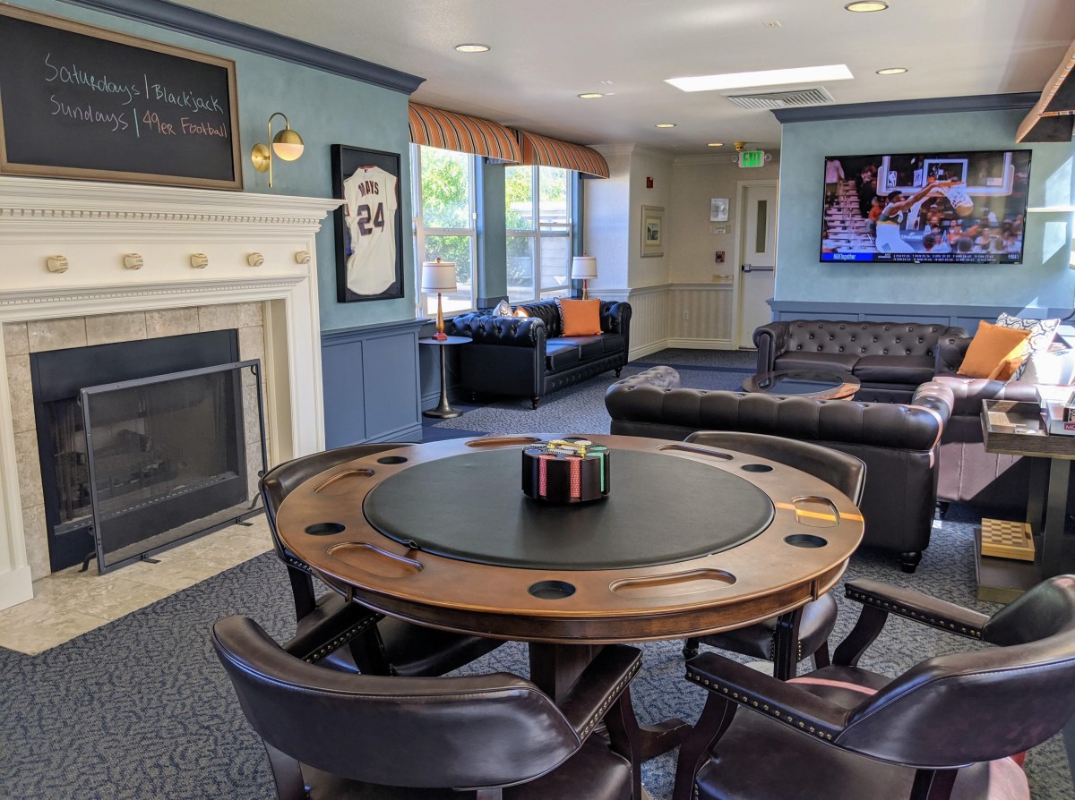 A cozy game room featuring a poker table, fireplace, and comfortable couches with a television mounted on the wall.