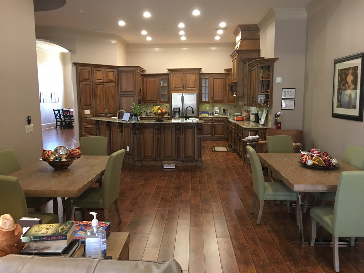 A modern kitchen with wood flooring, featuring an island and dining tables surrounded by chairs.