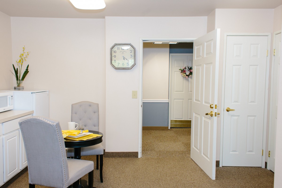 A small dining area with a table set for two, featuring an open door and a wall clock.