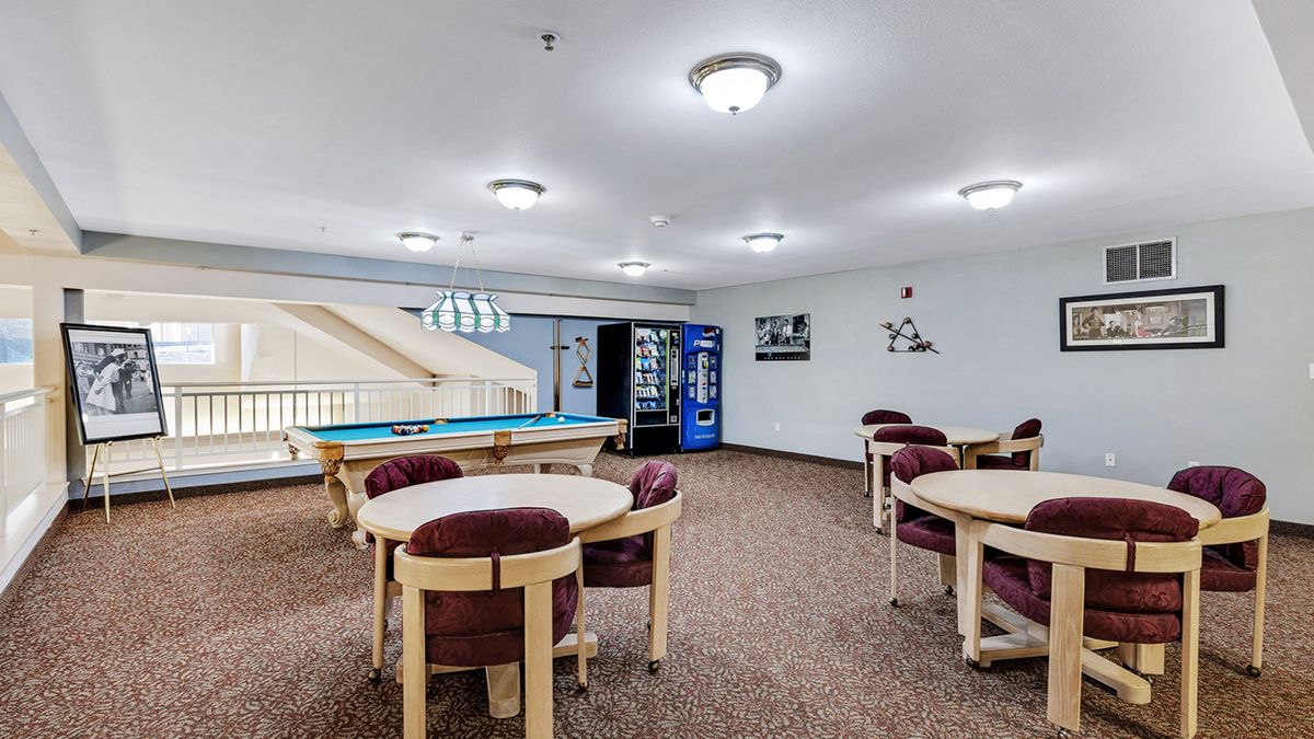 A spacious game room featuring a pool table, tables with chairs, and a vending machine under bright indoor lighting.