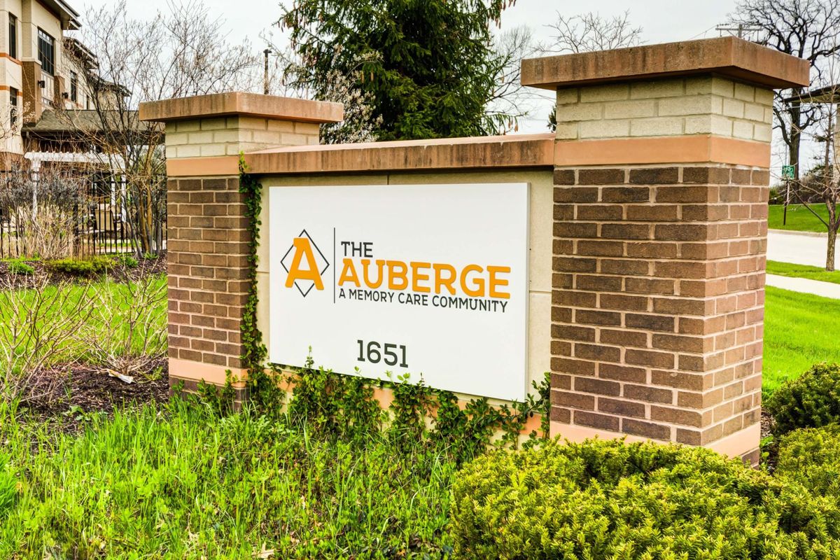 Sign for The Auberge luxury lake community on a brick wall.