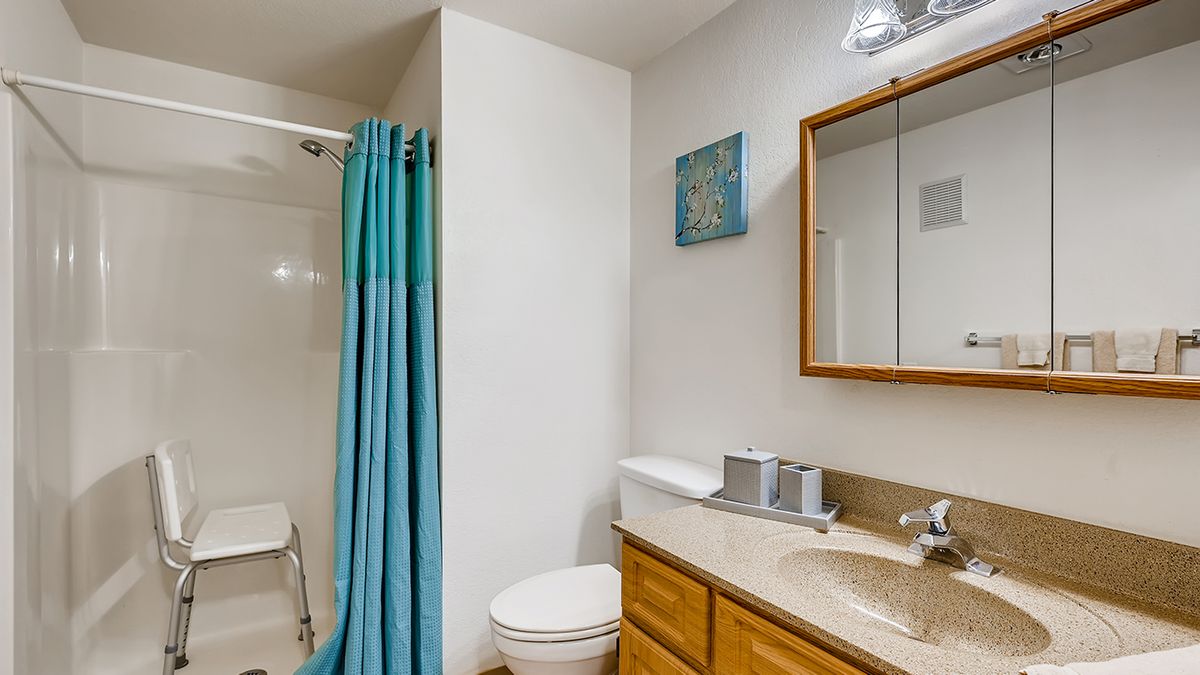 A clean and tidy bathroom with a shower, sink, mirror, and turquoise accents.
