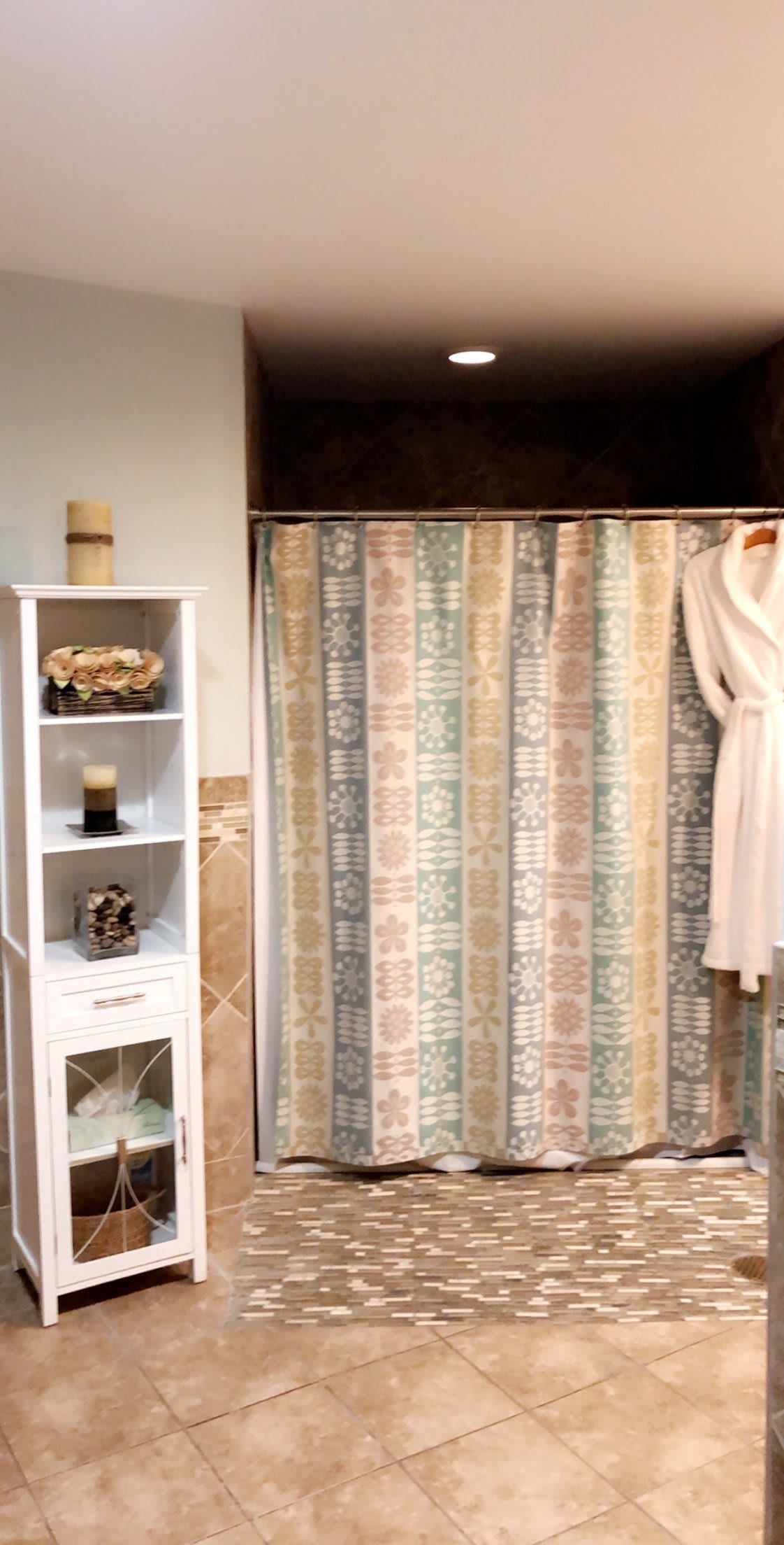 A cozy bathroom with a patterned shower curtain and a neatly organized white shelf adorned with decor items.