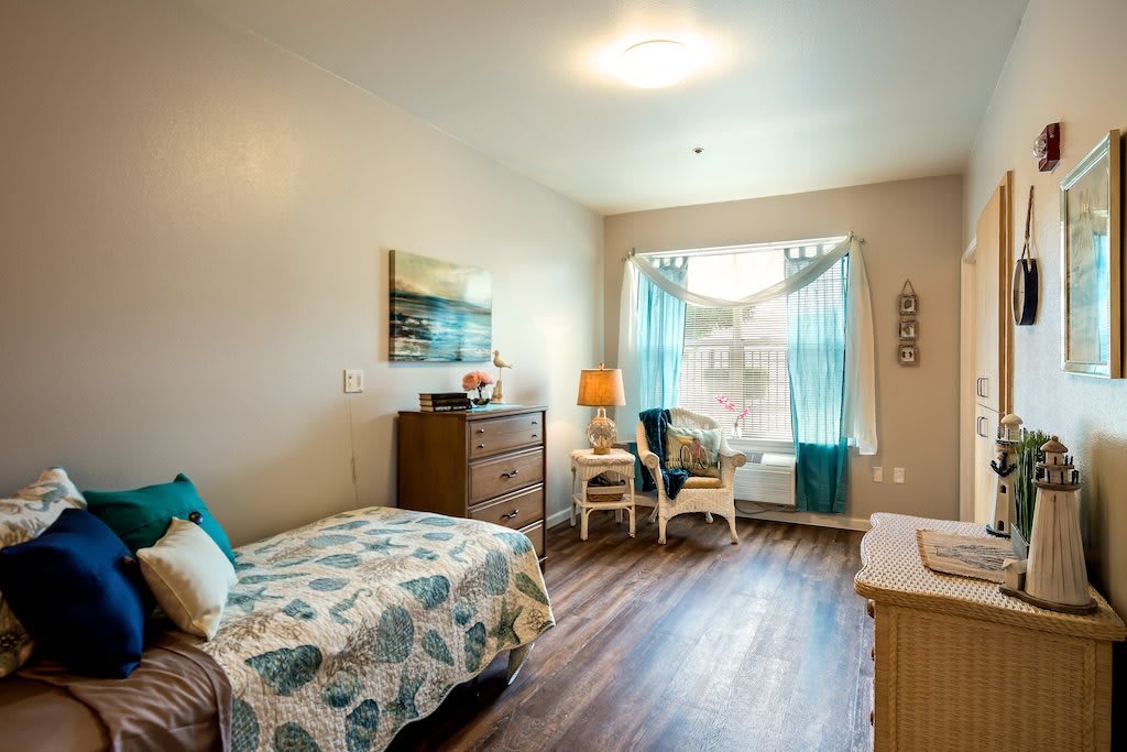 A cozy bedroom with a bed, dresser, and two chairs by a window.