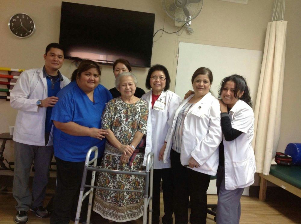 A group of healthcare professionals posing with an elderly person using a walker.