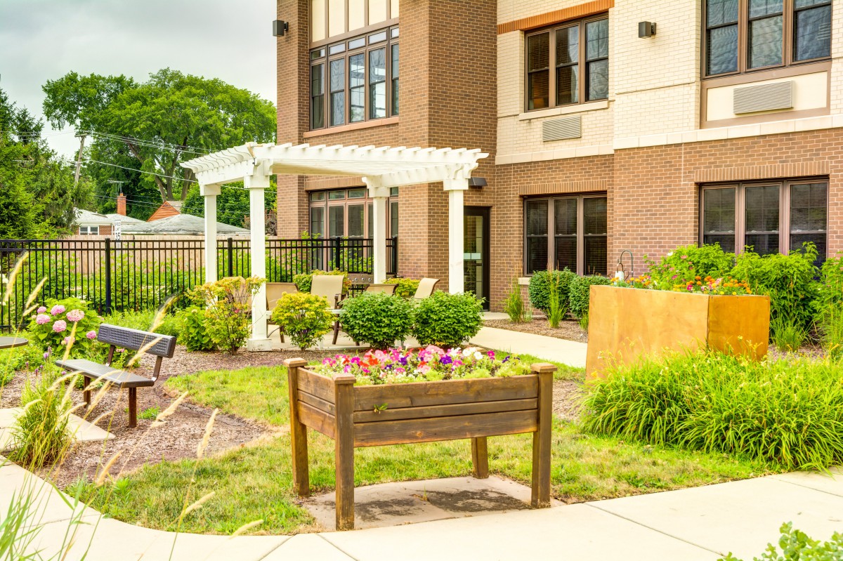 A well-maintained garden with a raised bed and pergola outside a modern building.