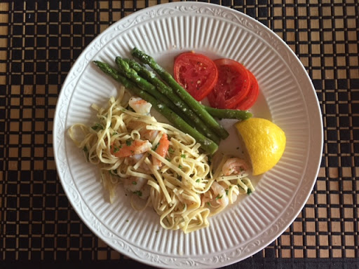 A delightful plate featuring pasta with shrimp, accompanied by asparagus, fresh tomato slices, and a lemon wedge.