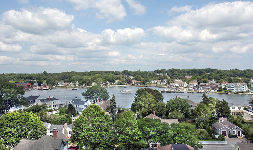 A scenic view of a riverside town with lush green trees and houses under a partly cloudy sky.