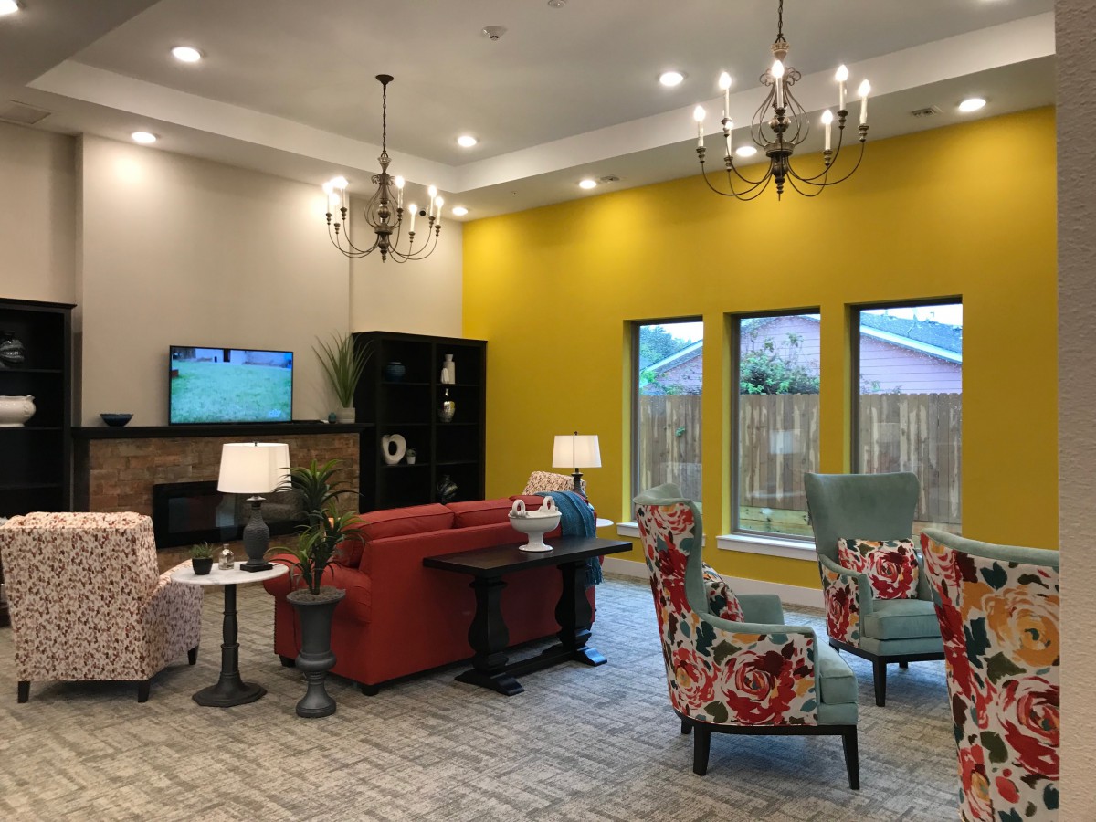 A cozy living room with vibrant decor, featuring a red sofa, patterned chairs, and a striking yellow accent wall.